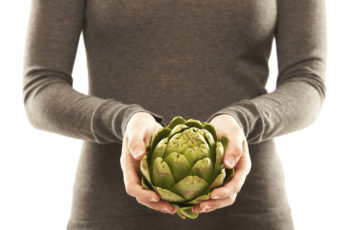 Mid section of a woman with an artichoke in her hands isolated o